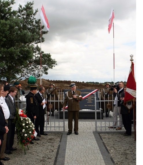Uroczystość odsłonięcia pomnika, przemawia żołnierz, obecne delegacje i flagi Polski