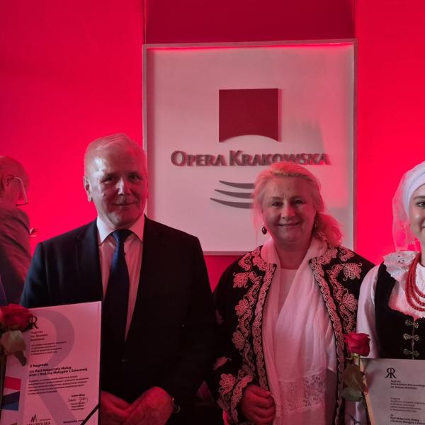 Czworo ludzi pozuje do zdjęcie. Kobiety po bokach ubrane w stroje ludowe z chustkami na głowie