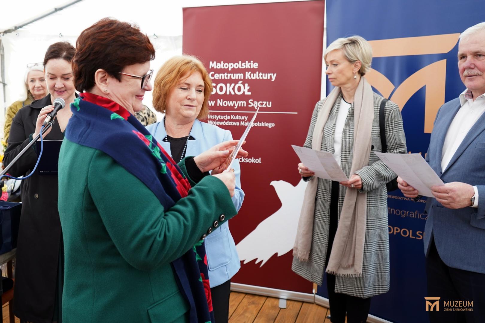 siwy mężczyzna wręcza dyplom starszej kobiecie w okularach